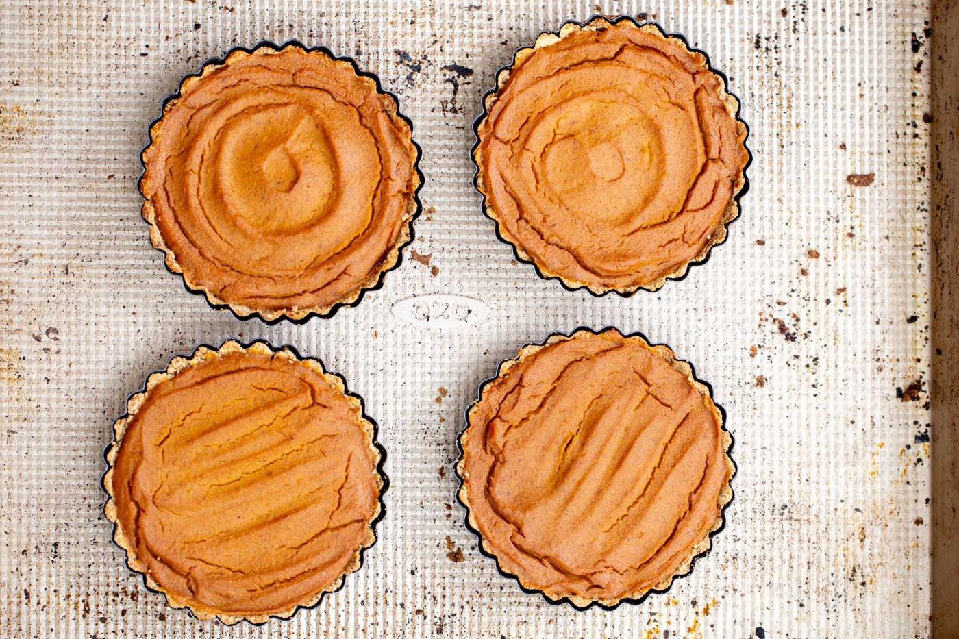 four gluten free vegan pumpkin pies on a baking sheet