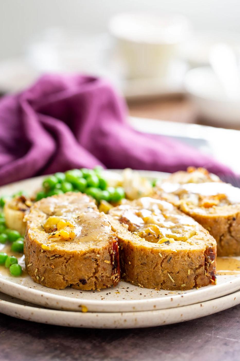 three slices of vegan glutenfree holiday loaf drizzled with gravy with a side of vegetables in the background