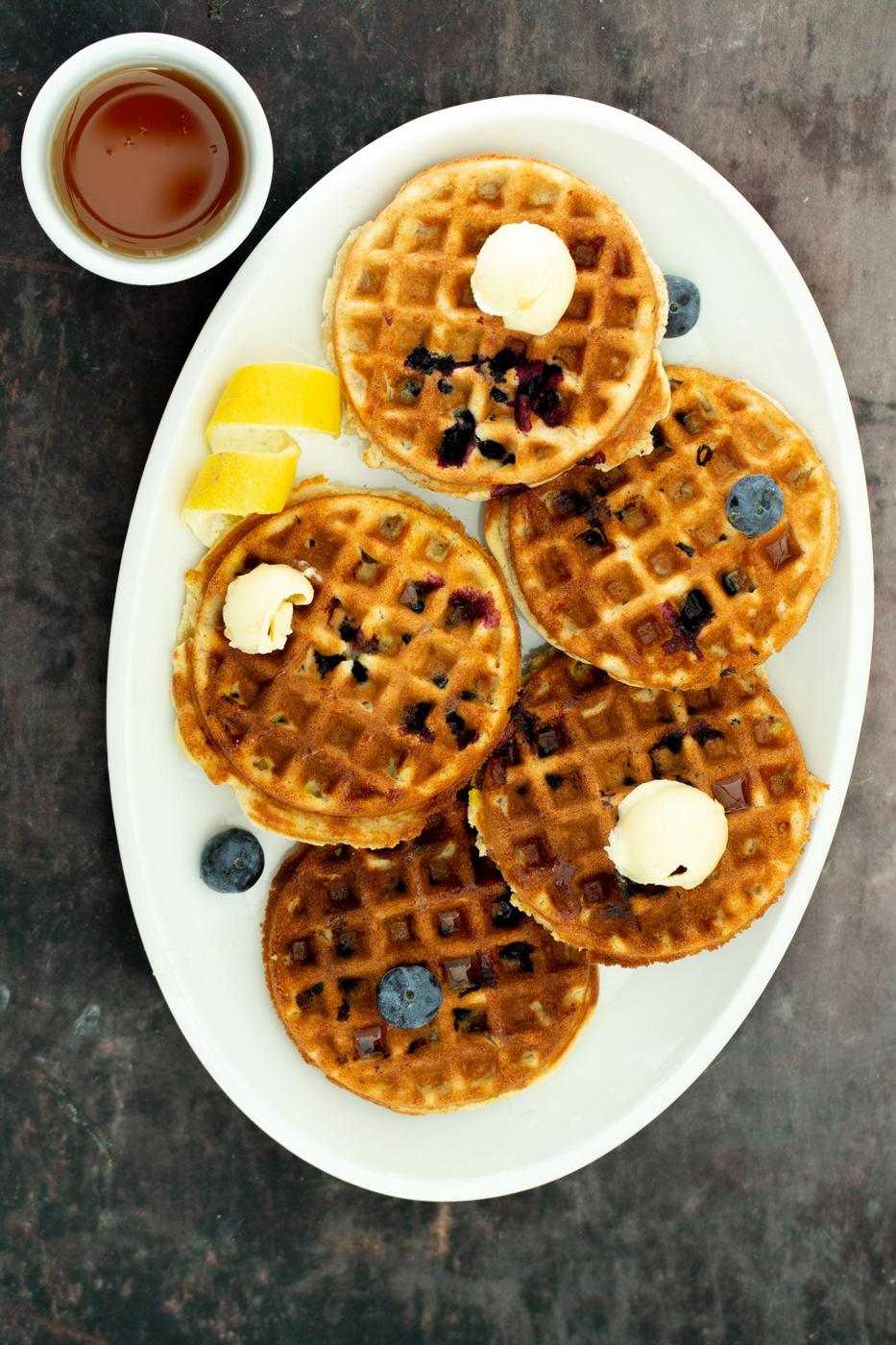 a white platter with glutenfree vegan lemon blueberry waffles served with a side dish of maple syrup