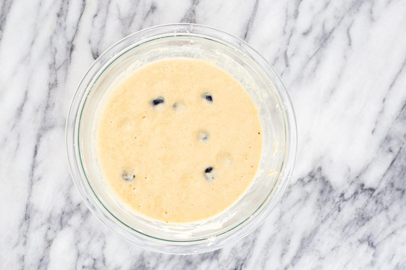 a glass bowl with glutenfree waffle batter with blueberries and lemon zest