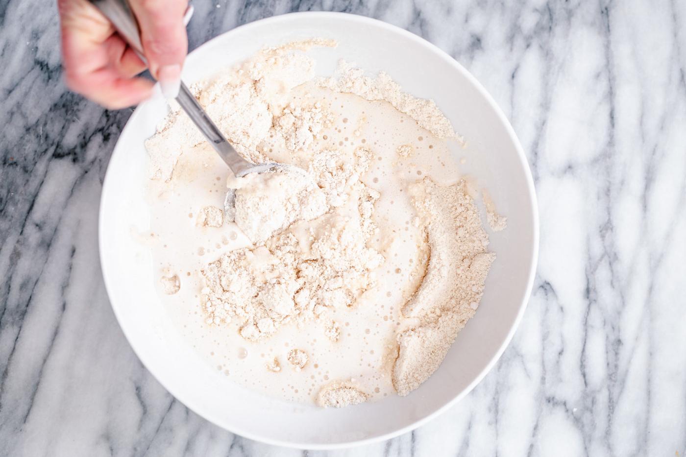 wet ingredients being stirred into dry donut ingredients in a white bowl