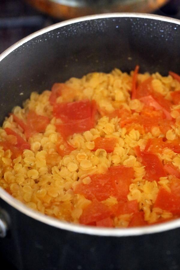 cooked red lentils and tomatoes simmering in a black saucepan to make lentil hummus