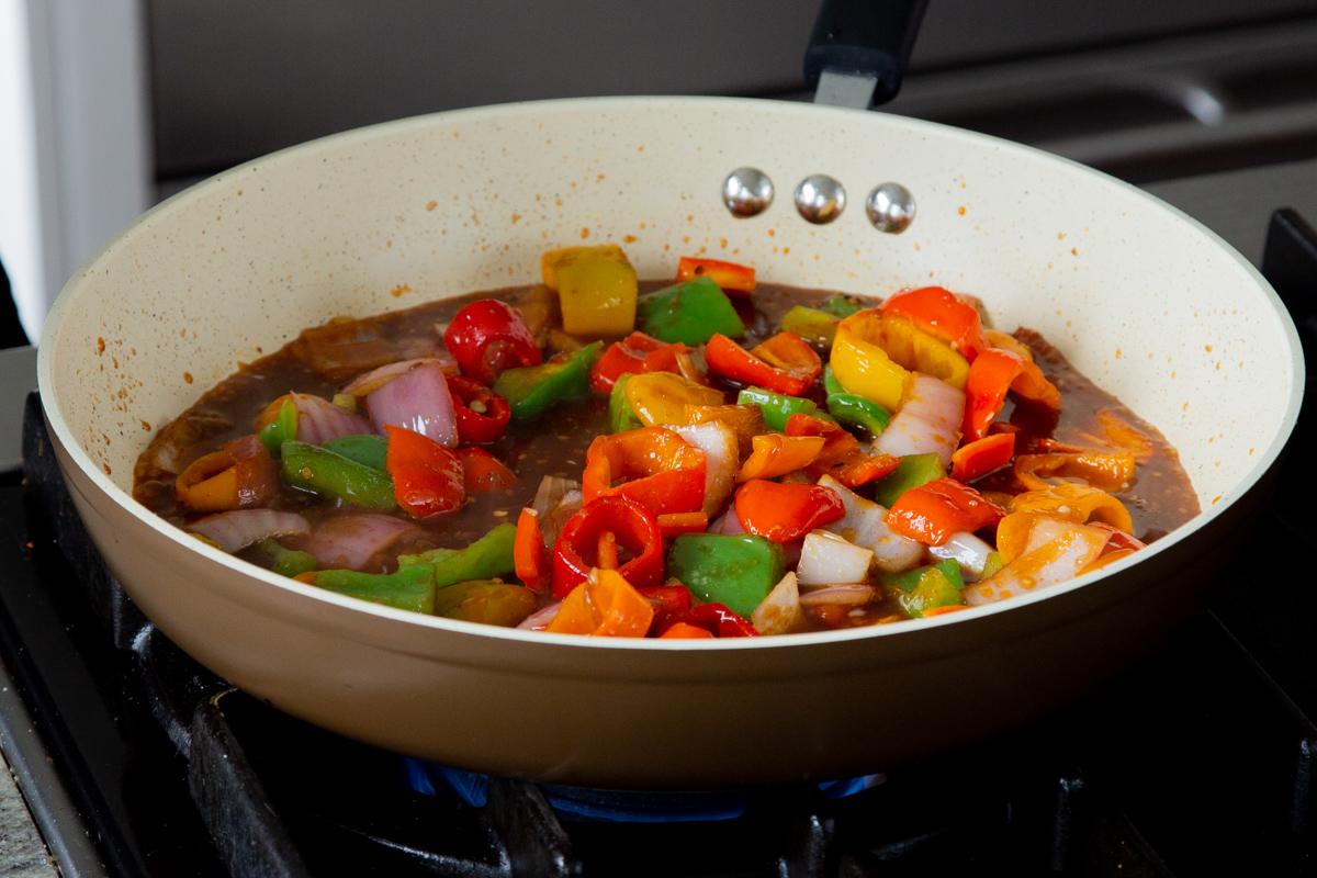 peppers and onions in the frying pan with gochujang and other sauces added, after mixing