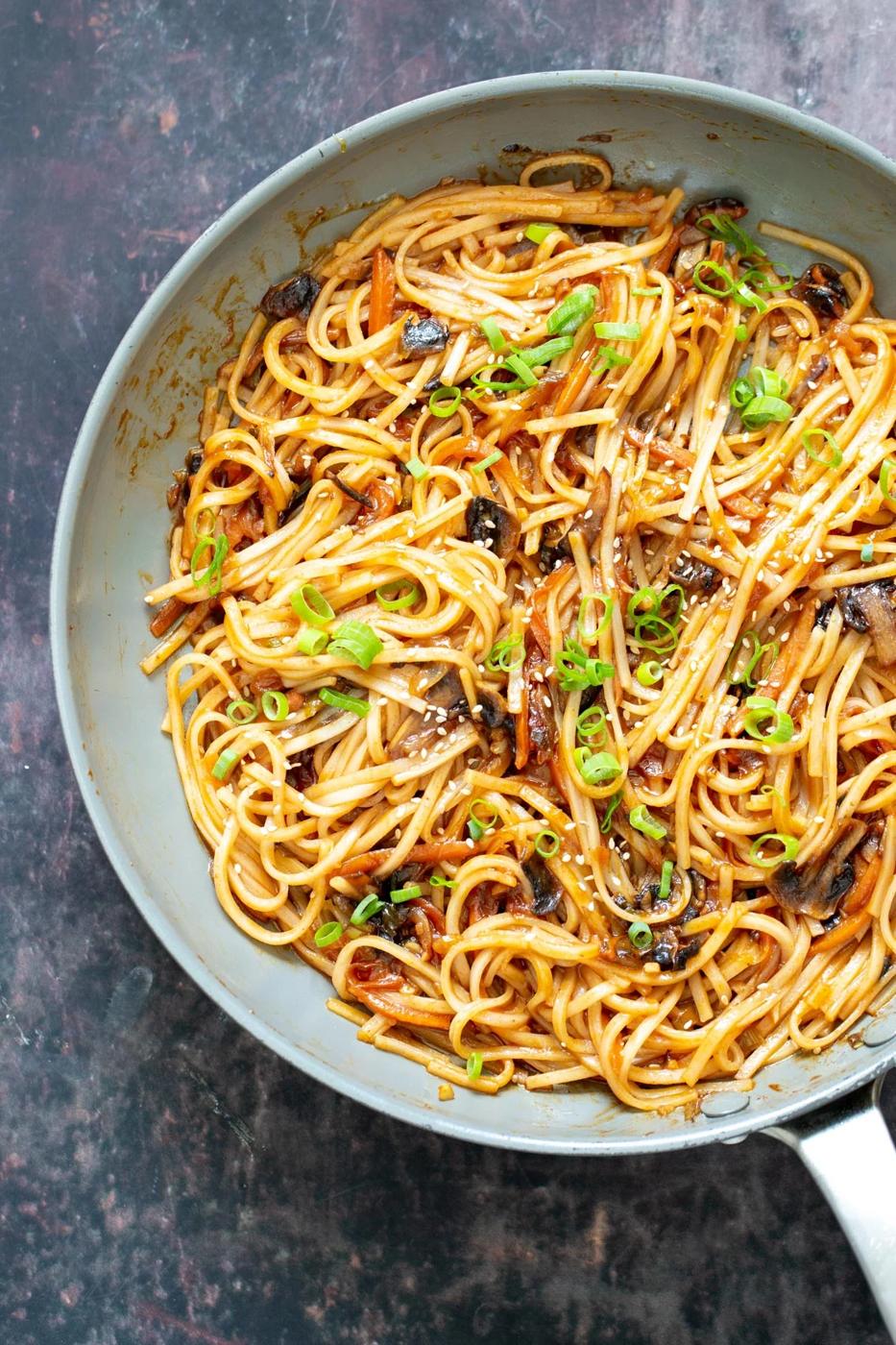 a saucepan with gochujang noodles with mushrooms and sliced spring onions