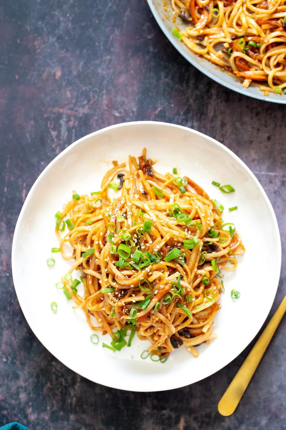 a plate of gochujang noodles topped with sliced spring onions and sesame seeds