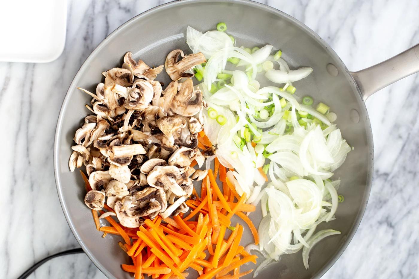 sliced onions, carrots, mushrooms and spring onions in a saucepan