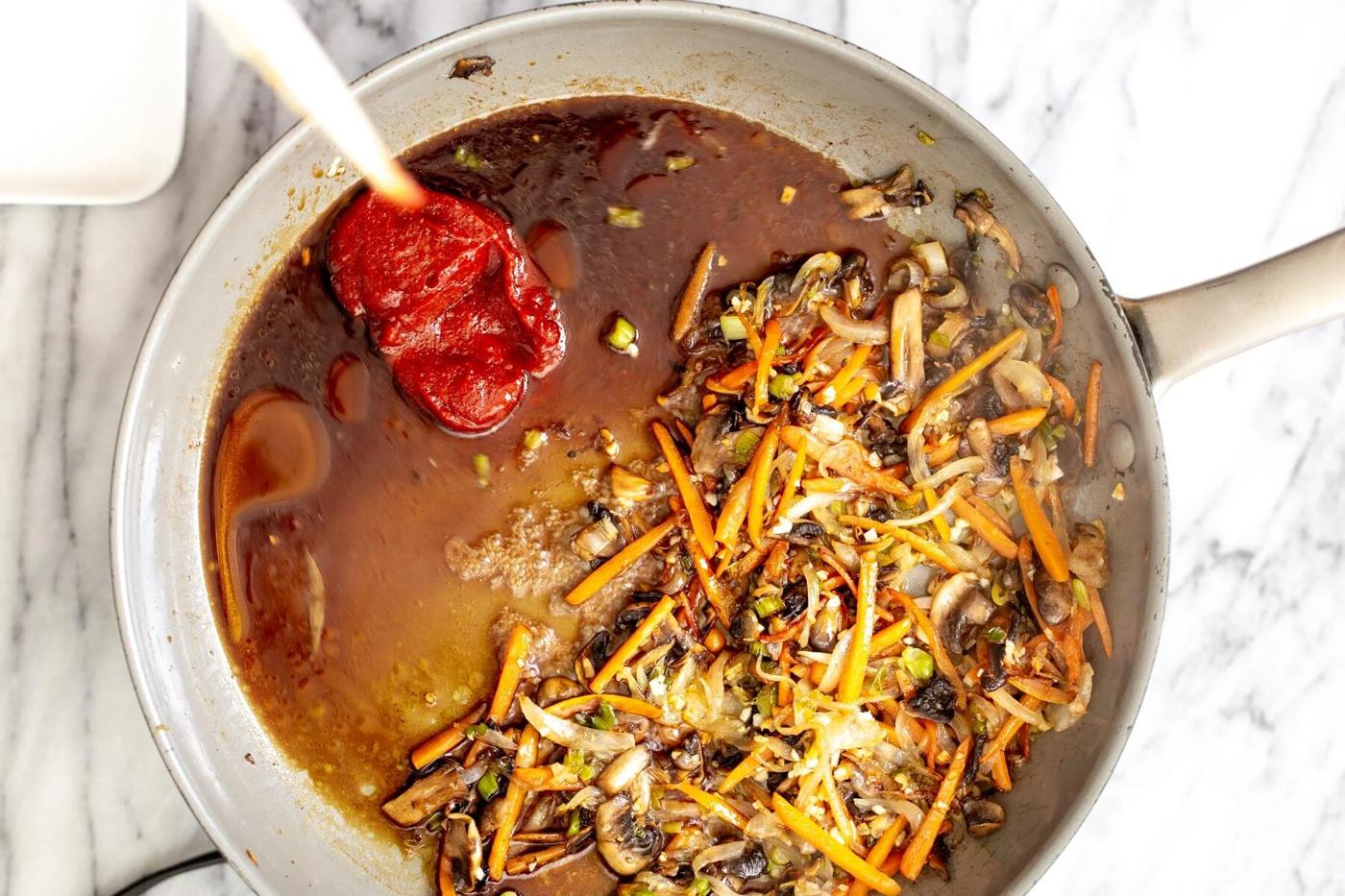 sauce ingredients for gochujang sauce being added to sauteed veggies in a saucepan
