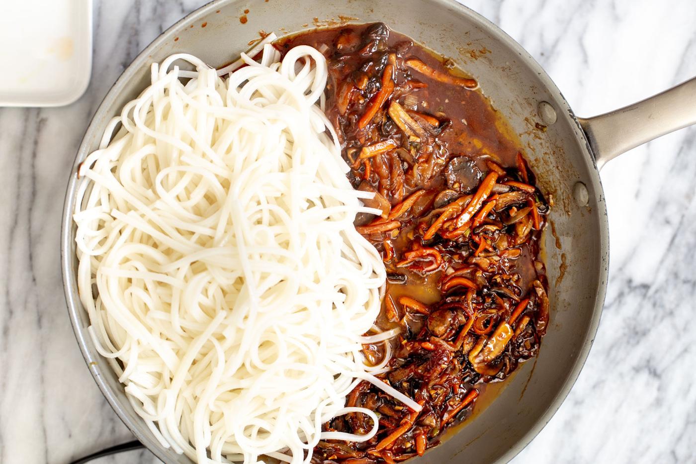 cooked rice noodles and veggies with Korean stir-fry sauce in a saucepan