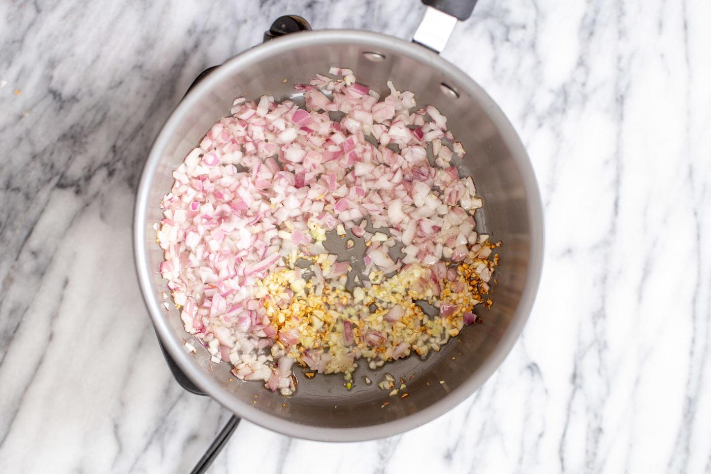 chopped onion, garlic and chile flakes being fried in a pot