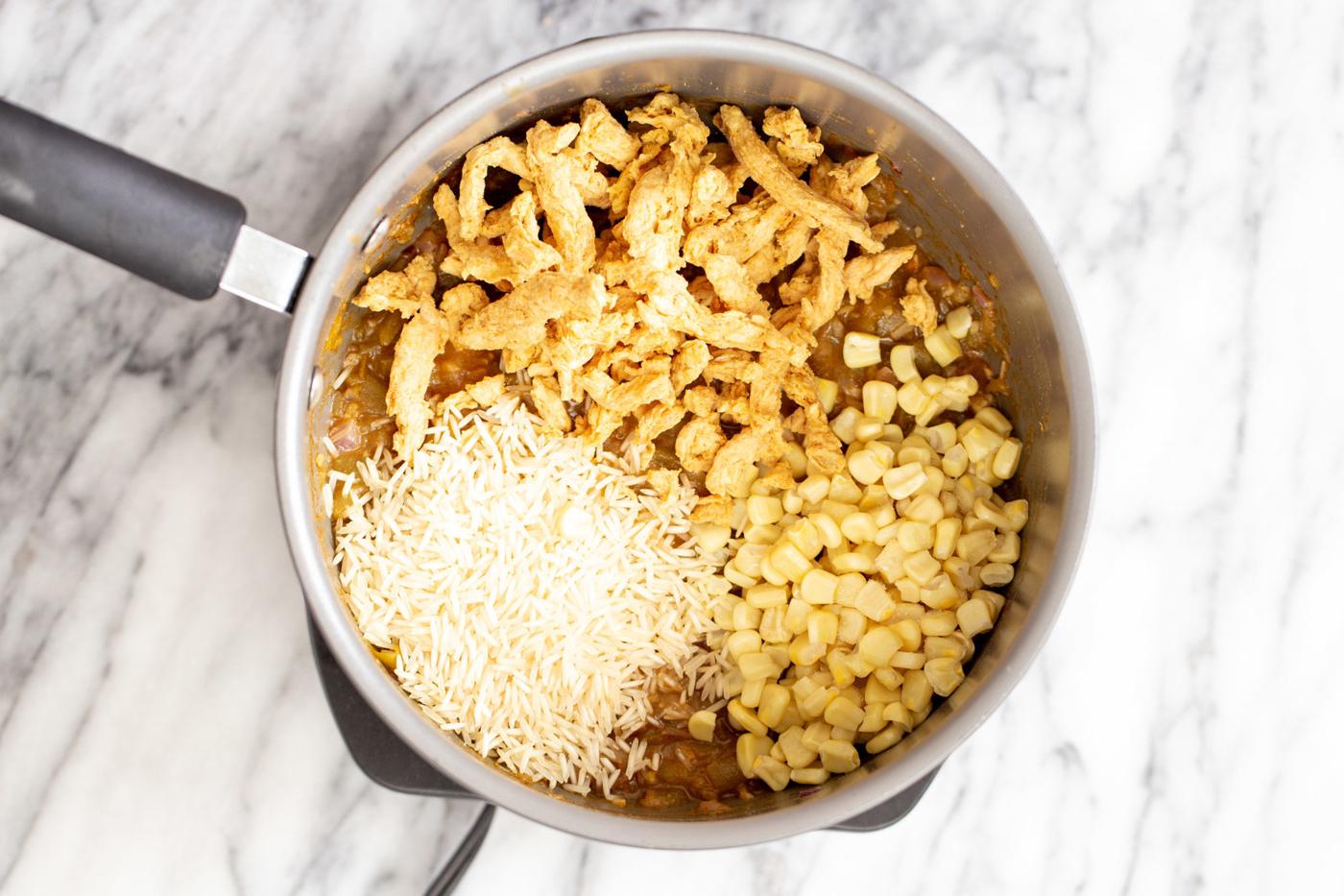 rice, soy chunks and corn being added to a pot with vegan enchilada soup