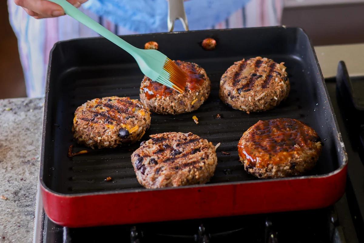 Five veggie burgers grilling in a pan.