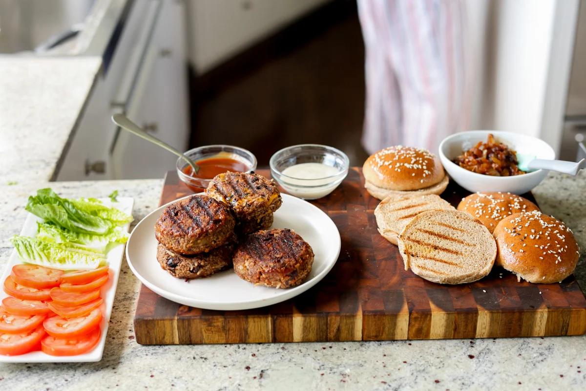 Buns, caramelized onions, and condiments on a wooden cutting board.