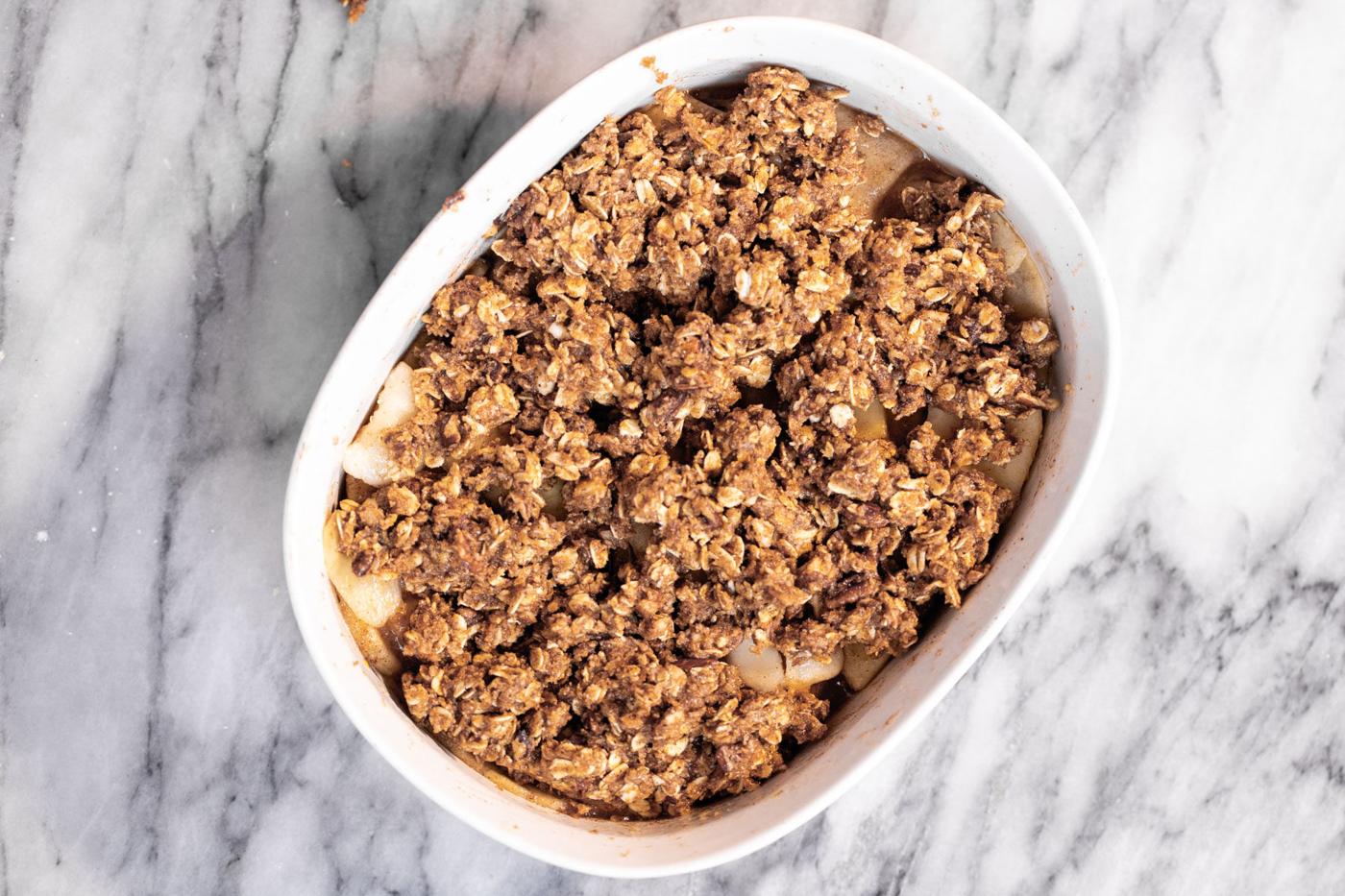 apple and pear slices being topped with crumble topping in a casserole dish