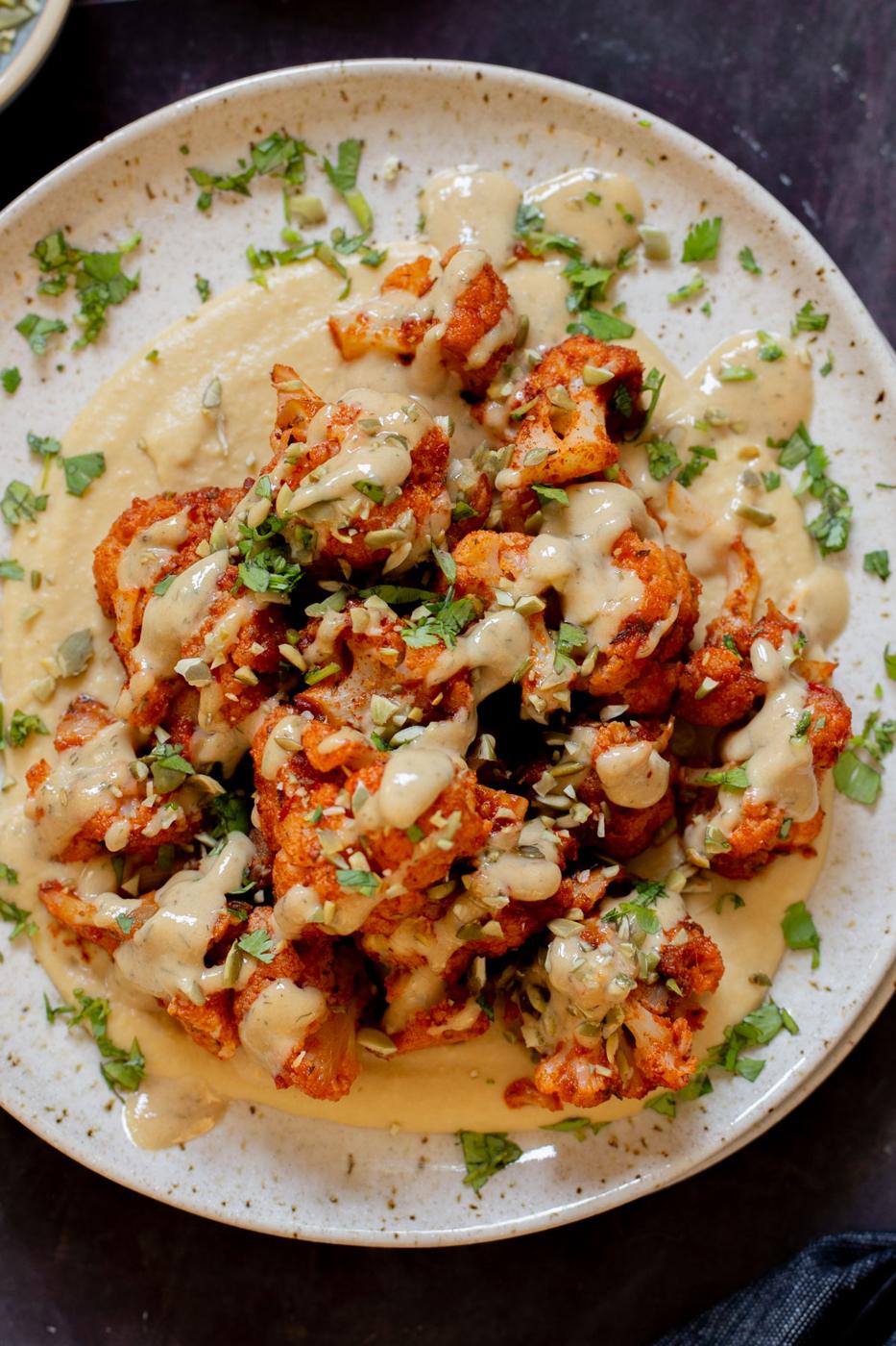 harissa cauliflower on a plate with hummus and tahini dressing
