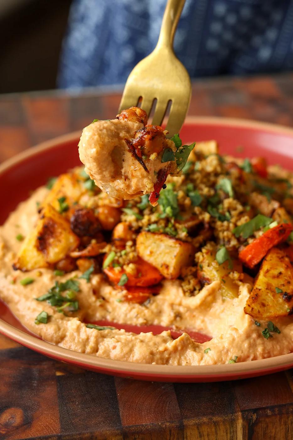 fork taking a bite of harissa bean puree topped with roasted vegetables and baharat walnuts