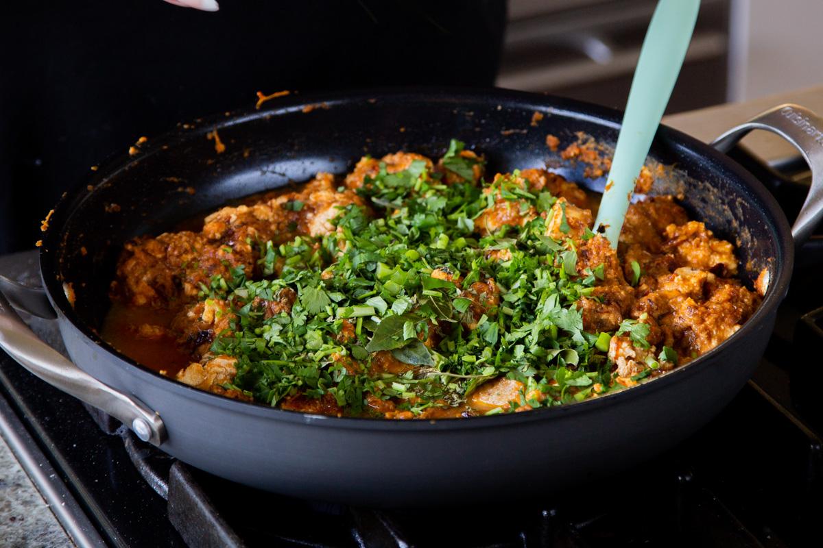 adding cilantro to the Hyderabadi chicken curry in the pan