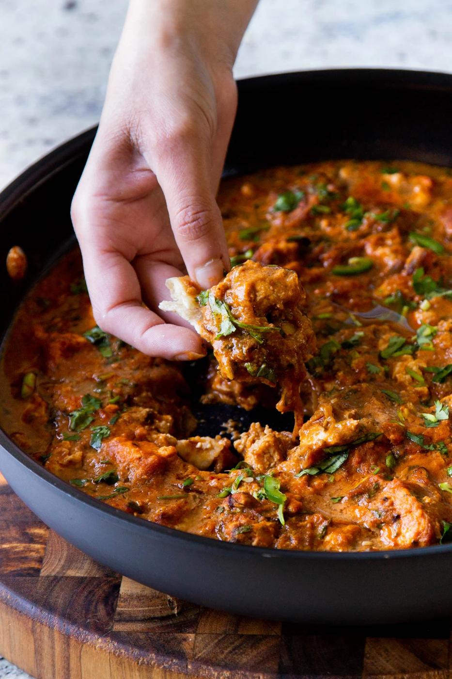 hand scooping up some Hyderabadi chicken curry on a piece of flatbread