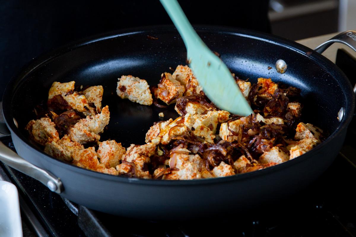 stirring the spiced tofu to the pan with the onions