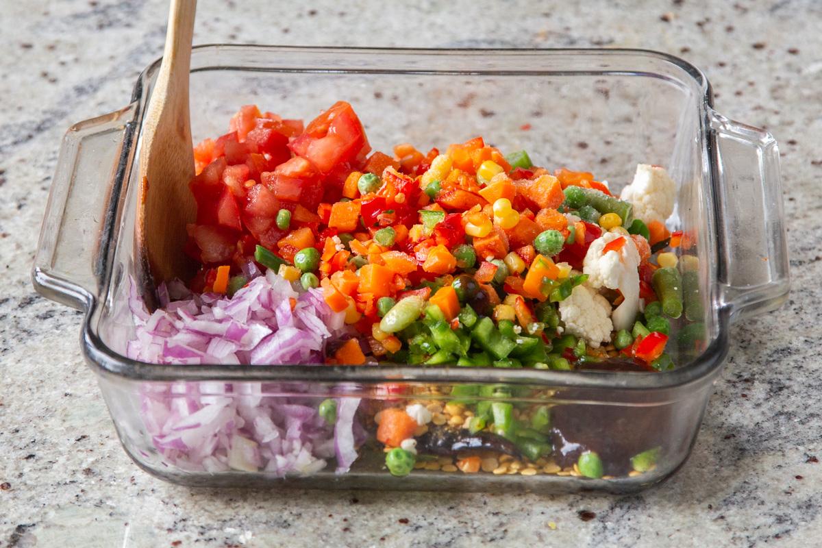 veggies being added to tempering in a glass casserole dish