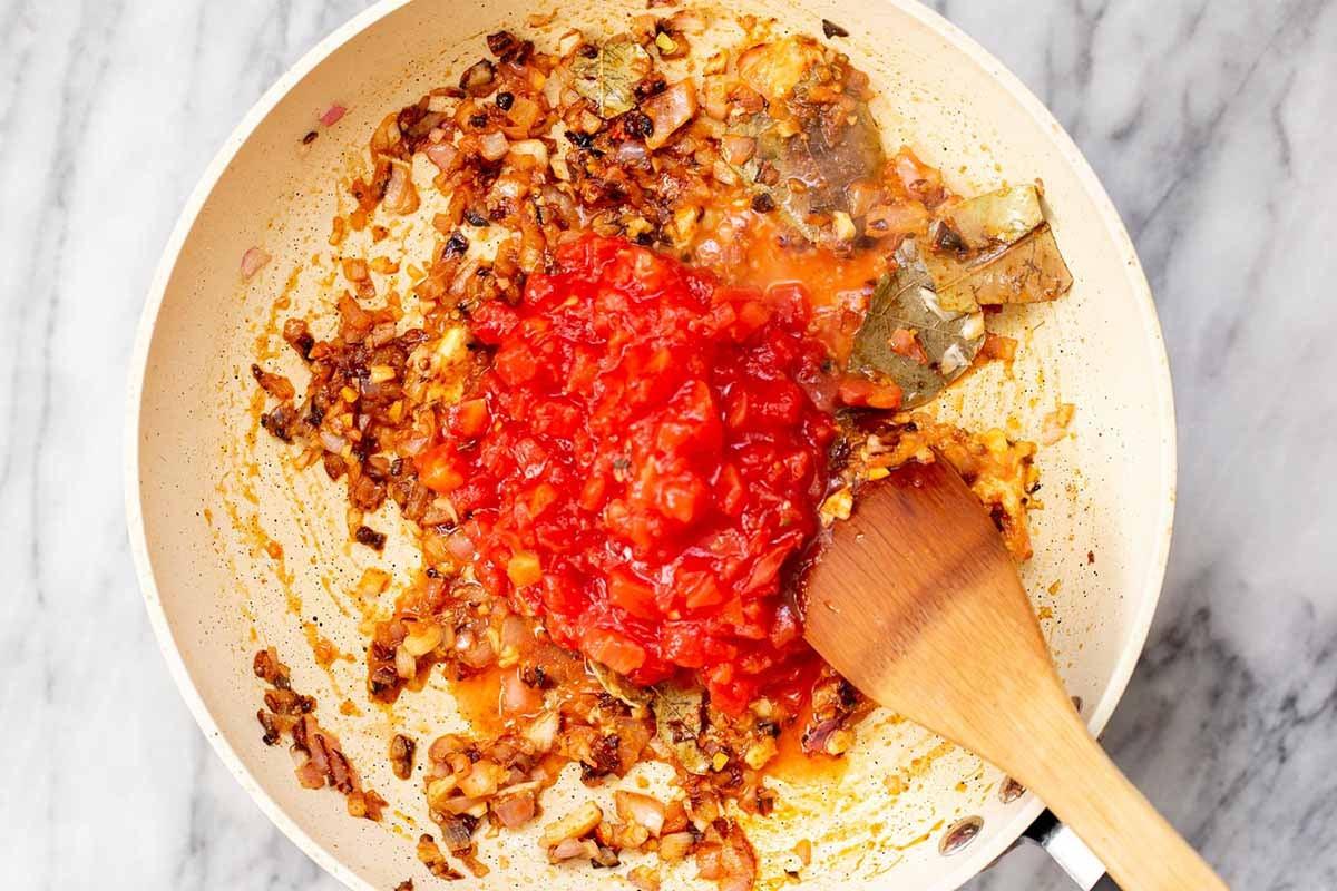 adding the tomato to the pan of cooked onion and whole spices