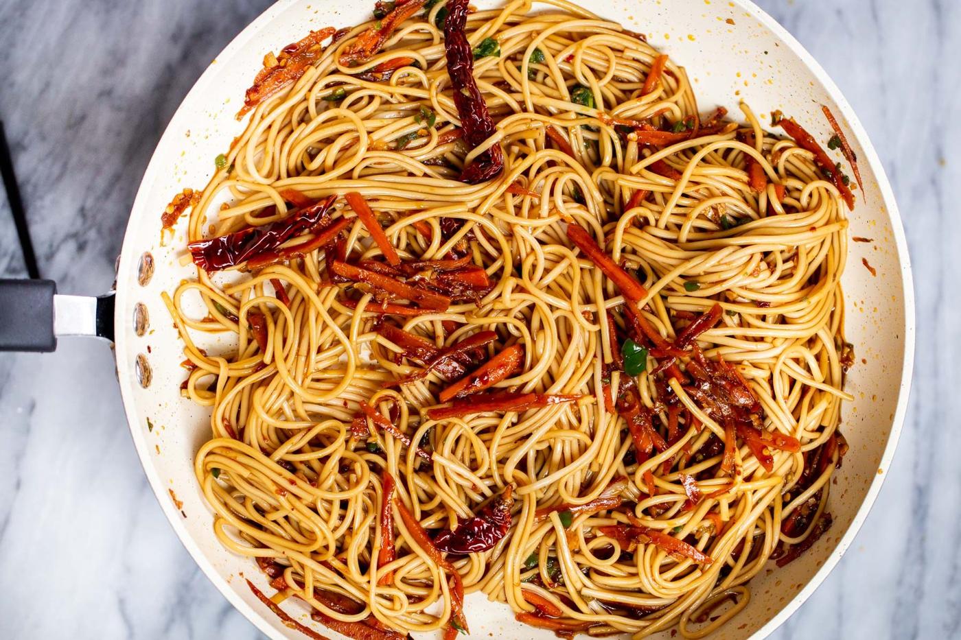 cooked lo mein noodles being tossed with sauce and sauteed veggies for making stir-fry
