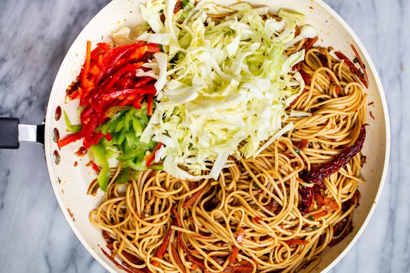 bell pepper and chopped cabbage being added to sauteeing pan with noodles