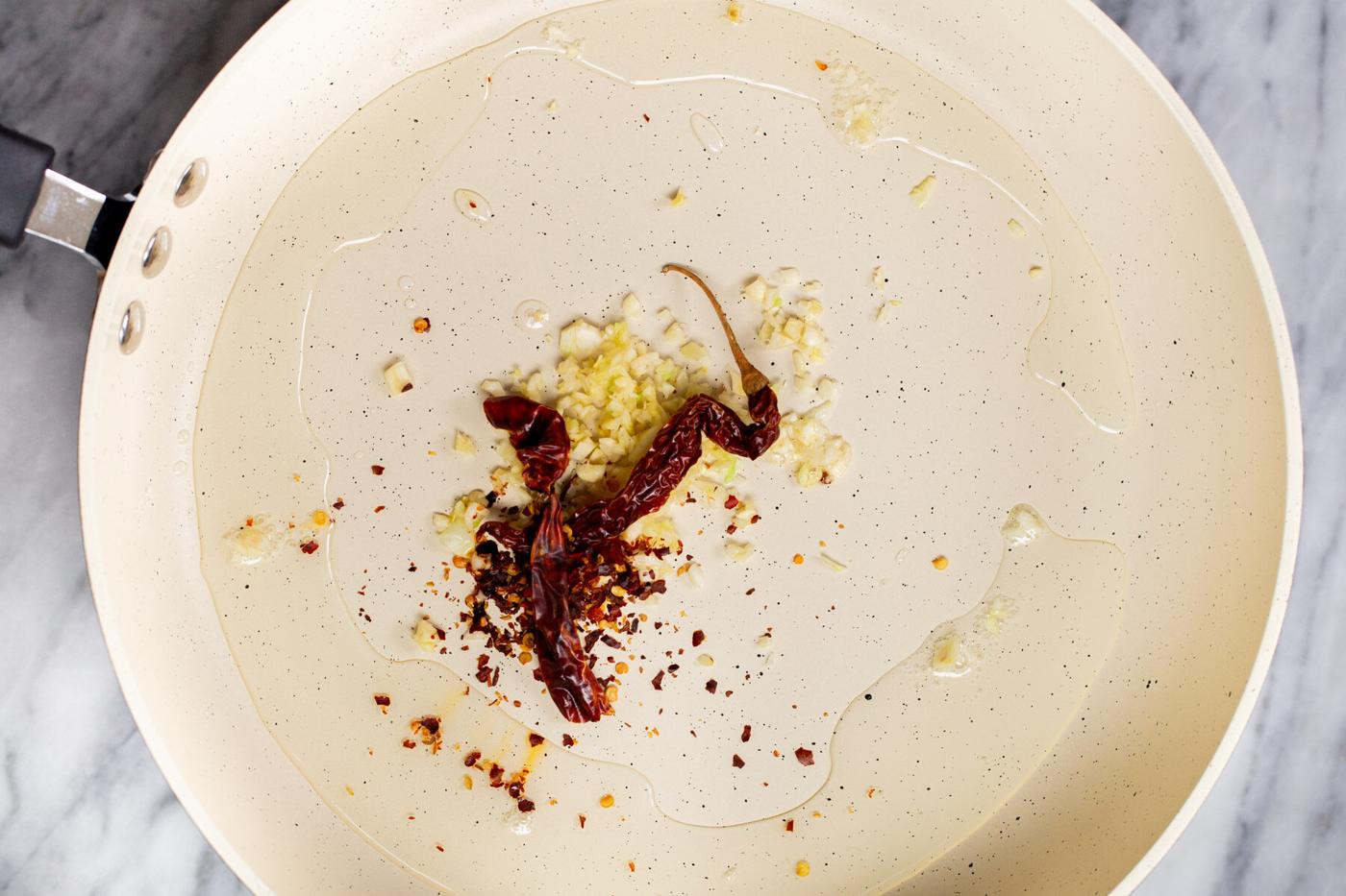 chili and garlic frying in oil in a white pan