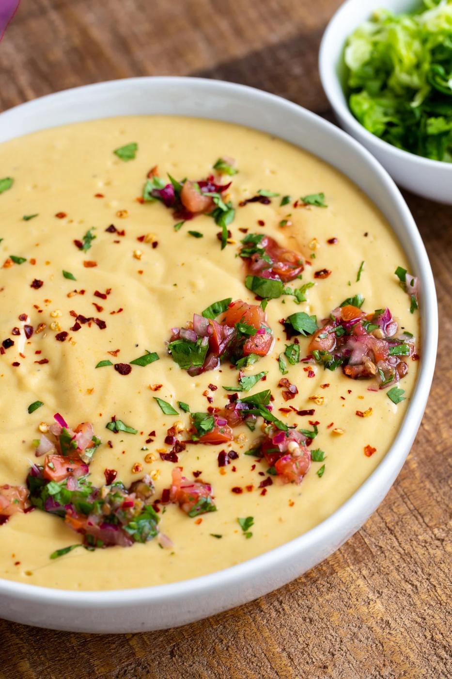a white bowl filled with Instant Pot Vegan Cheese Sauce decorated with fresh chopped herbs and tomatoes