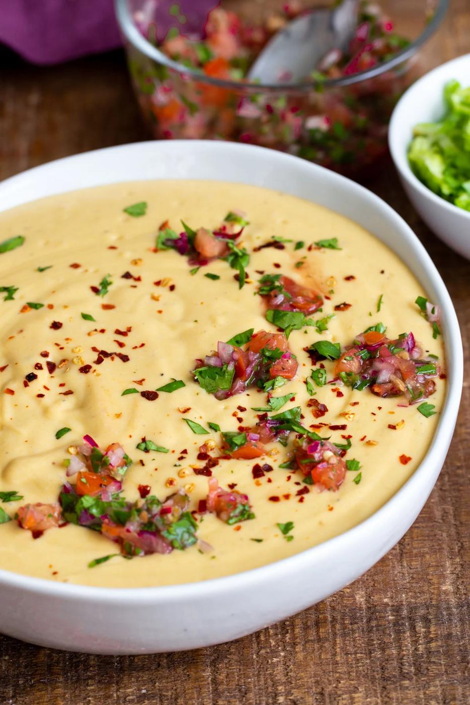 side view of a white bowl filled with vegan cheese sauce and sprinkled with herbs and chopped tomatoes