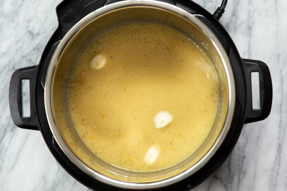 garlic being added to instant pot with vegan cheese sauce ingredients