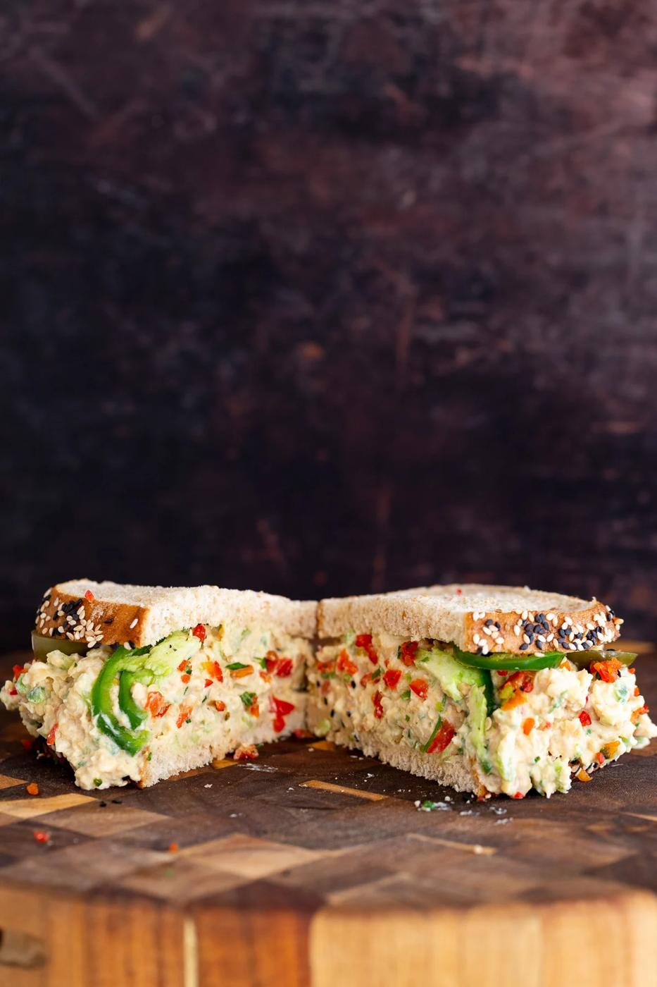 halfed vegan jalapeño popper chickpea salad sandwich on a wooden chopping board
