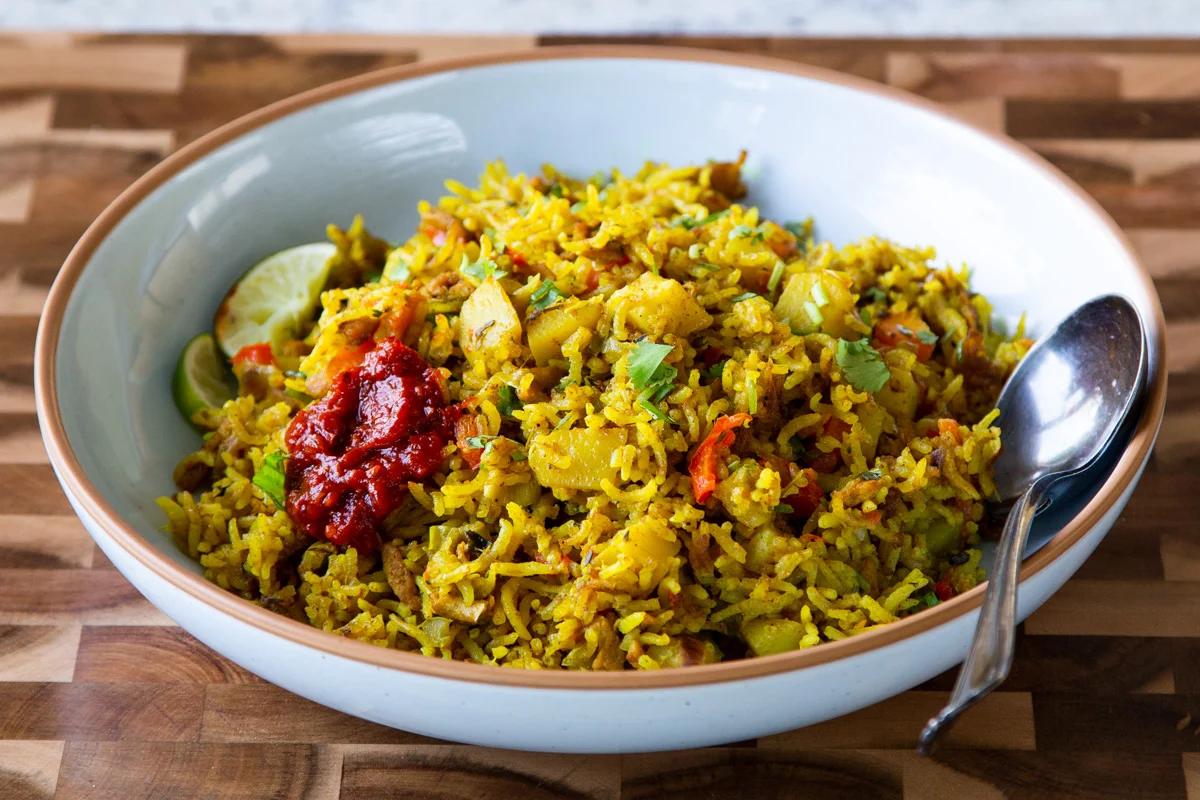 bowl of Jamaican curry rice with hot sauce and lime
