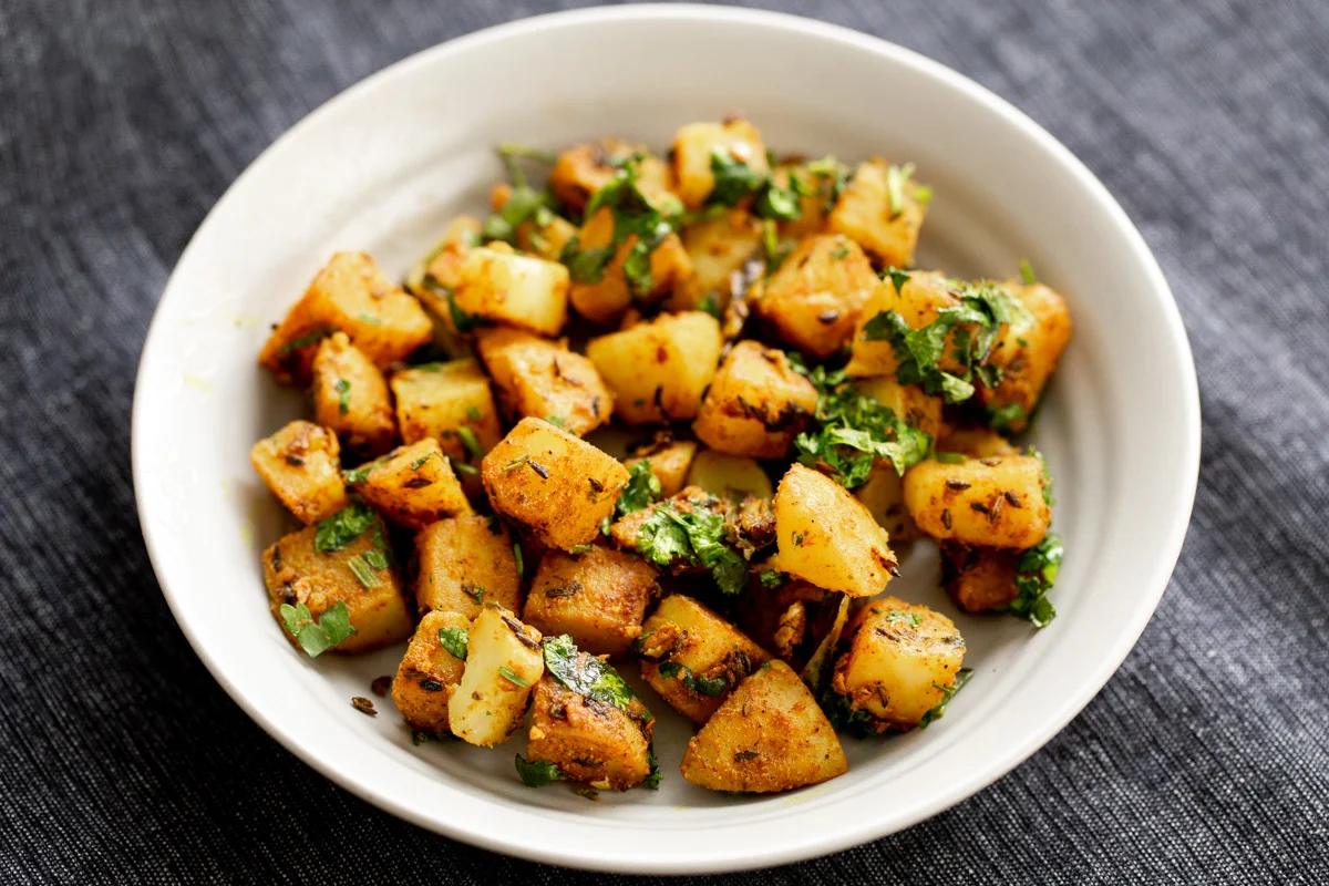 jeera aloo in a small white bowl topped with chopped cilantro