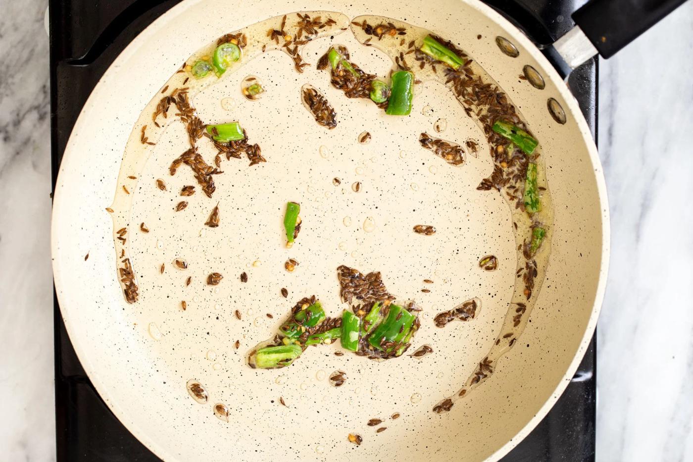 green chili and cumin seeds frying in a pan
