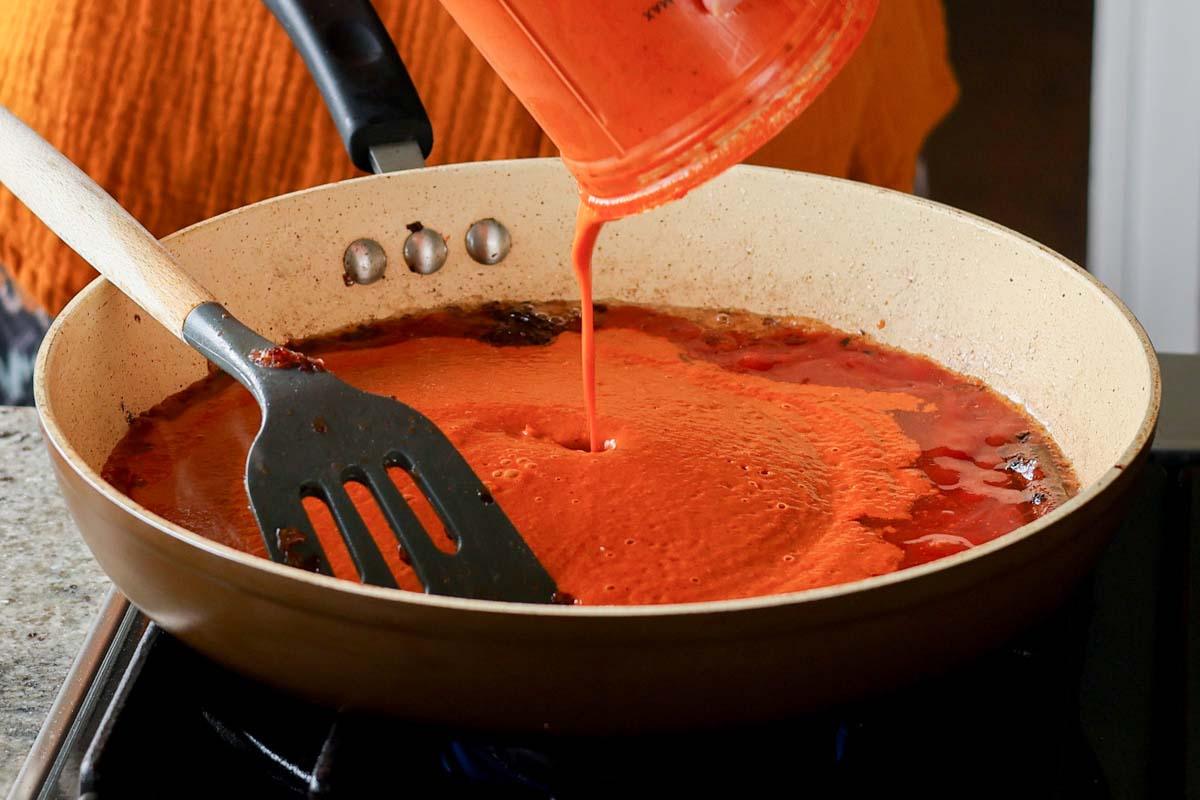 adding the blended tomato sauce to the pan