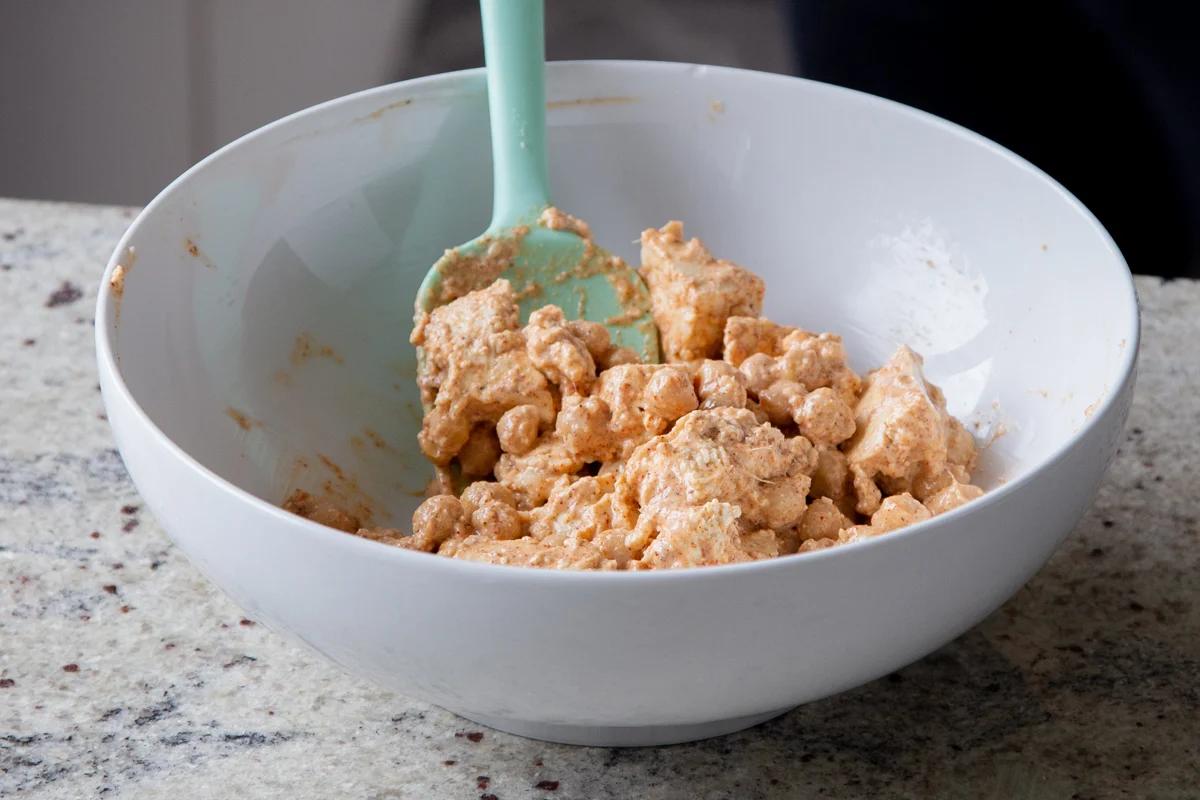 torn tofu and chickpeas in a bowl with non-dairy cream and spices added, after mixing