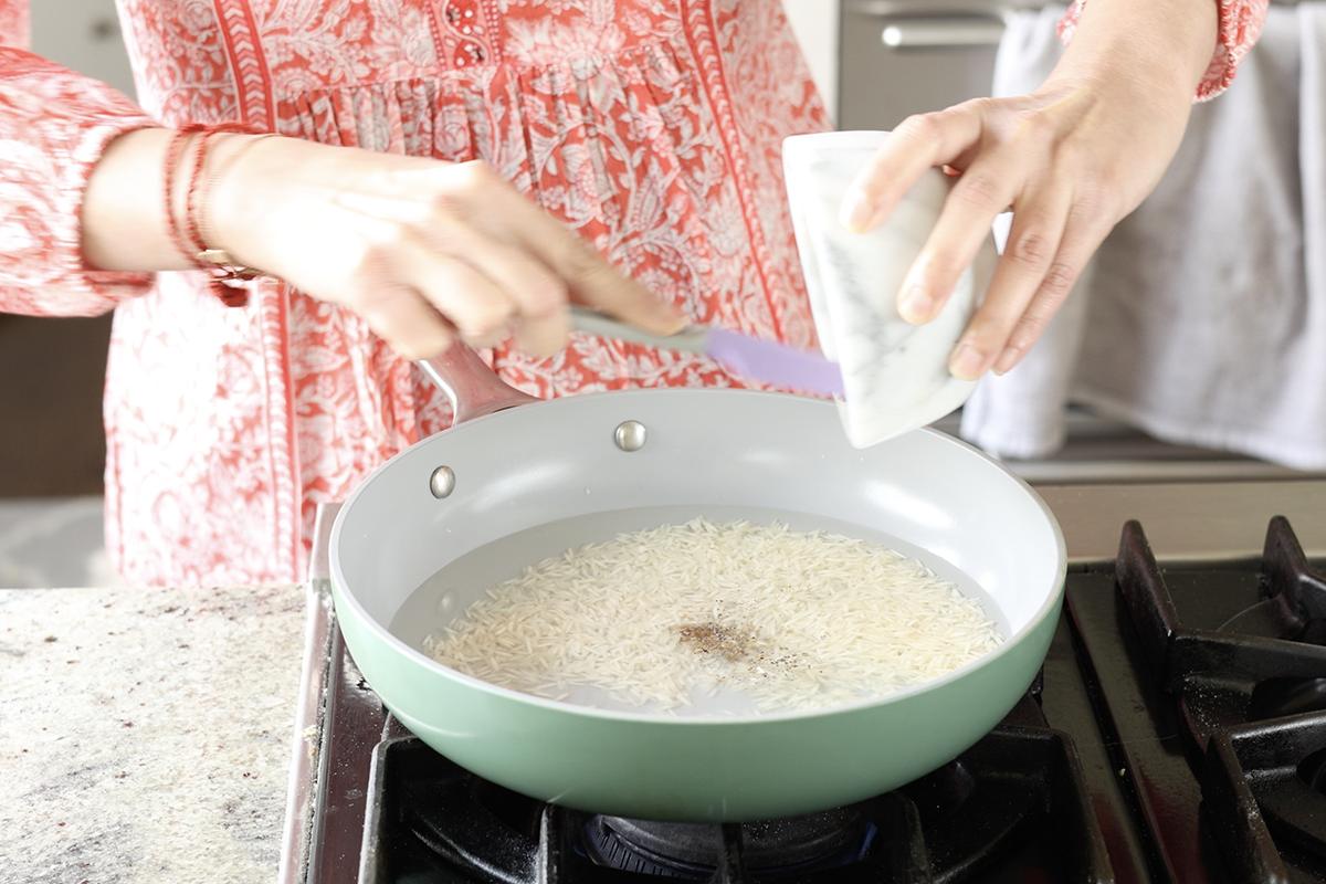 adding spices to the rice in the pan