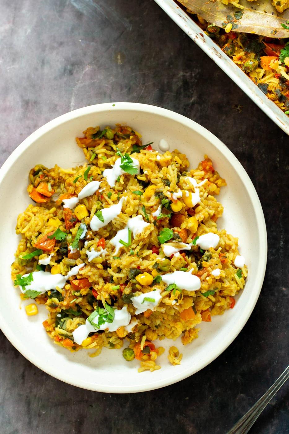 a plate of vegan baked kitchari lentil rice casserole served with fresh herbs and yogurt