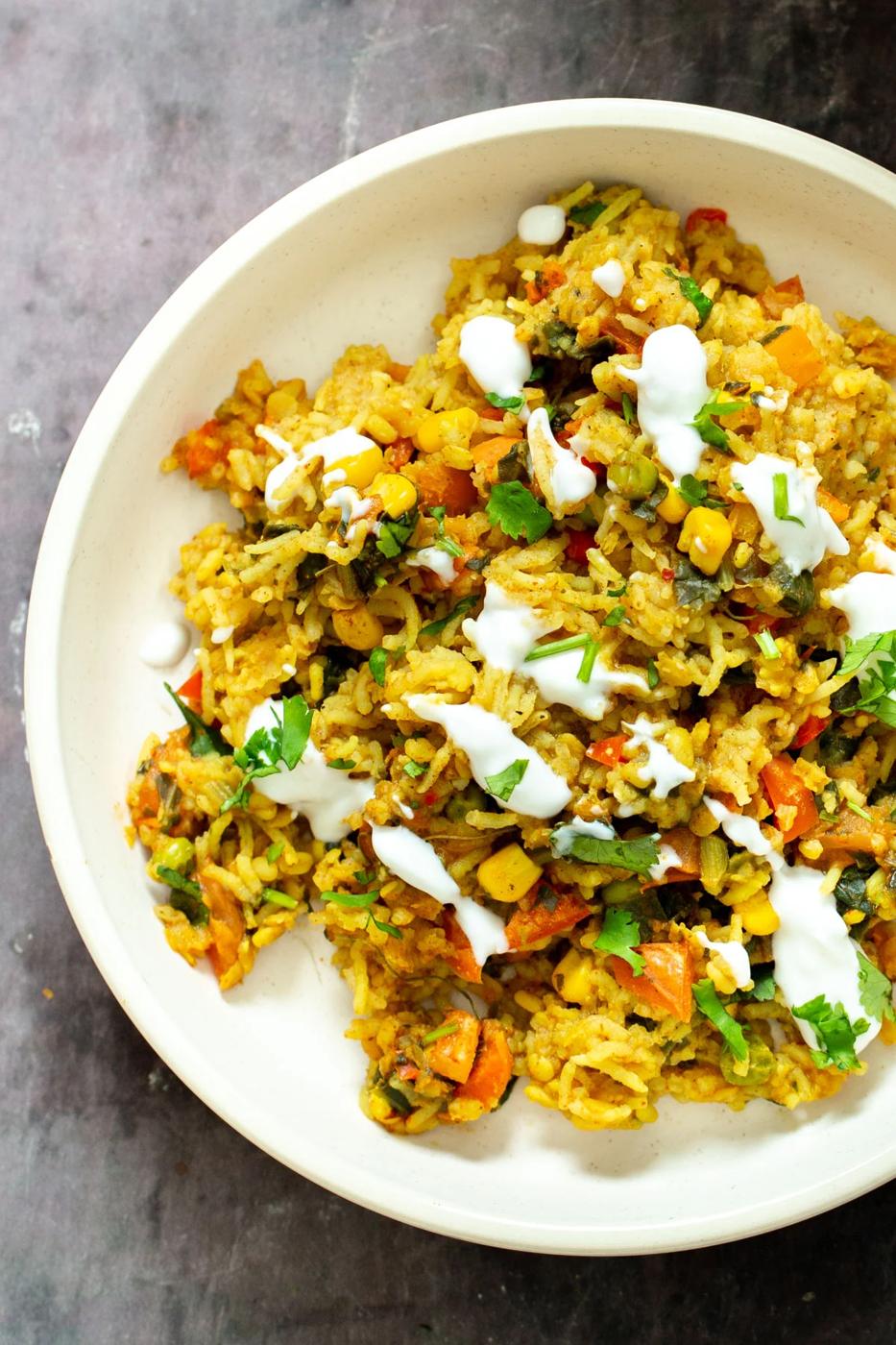 close up shot of a plate of Indian lentil rice casserole drizzles with vegan yogurt