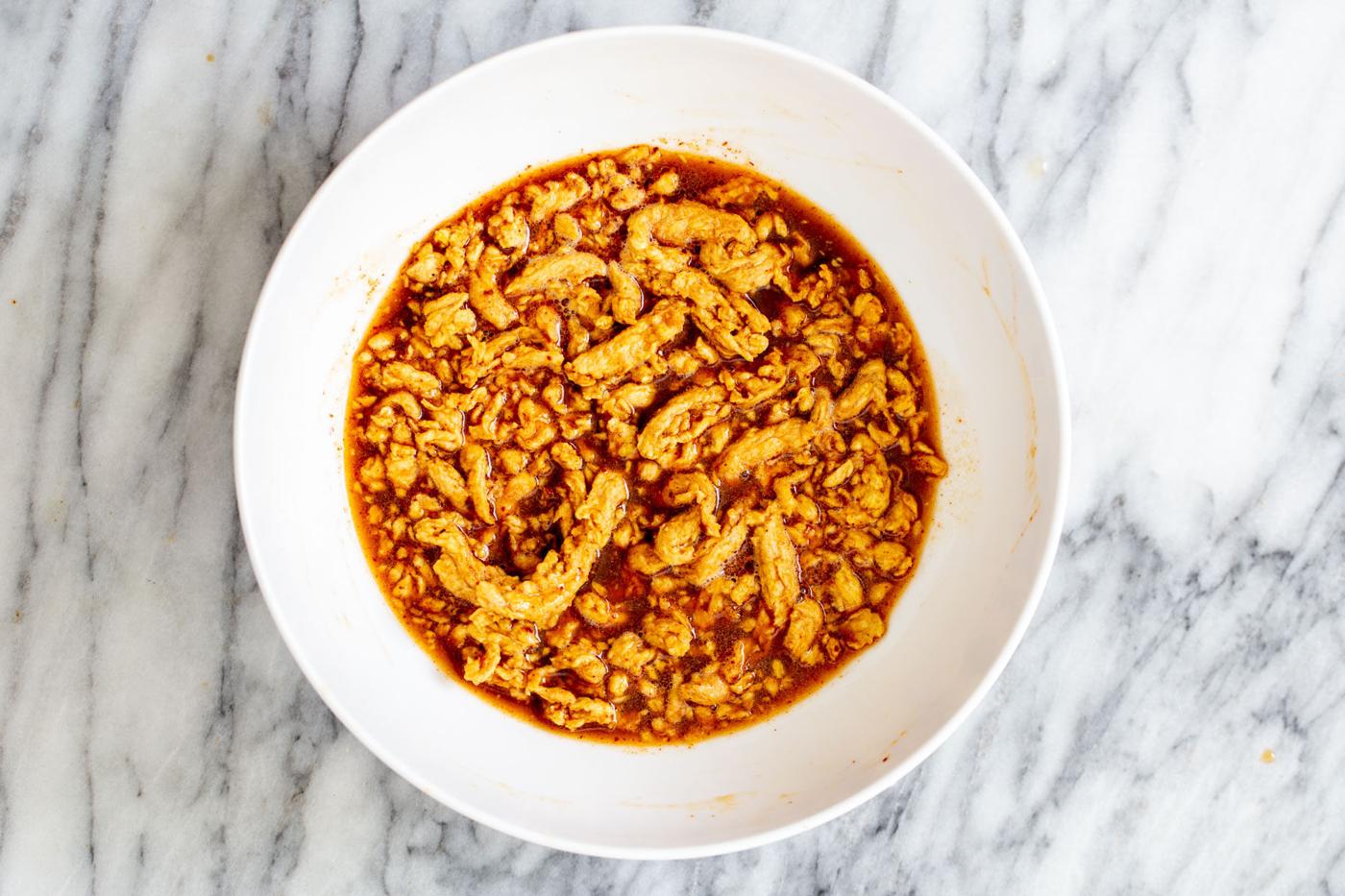 soy curls being marinated in korean bbq marinade in a white bowl