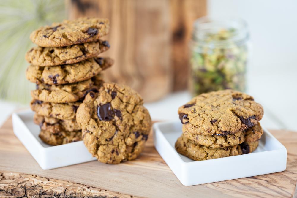 stack of chocolate chunk pistachio cookies on two white plates on wooden board