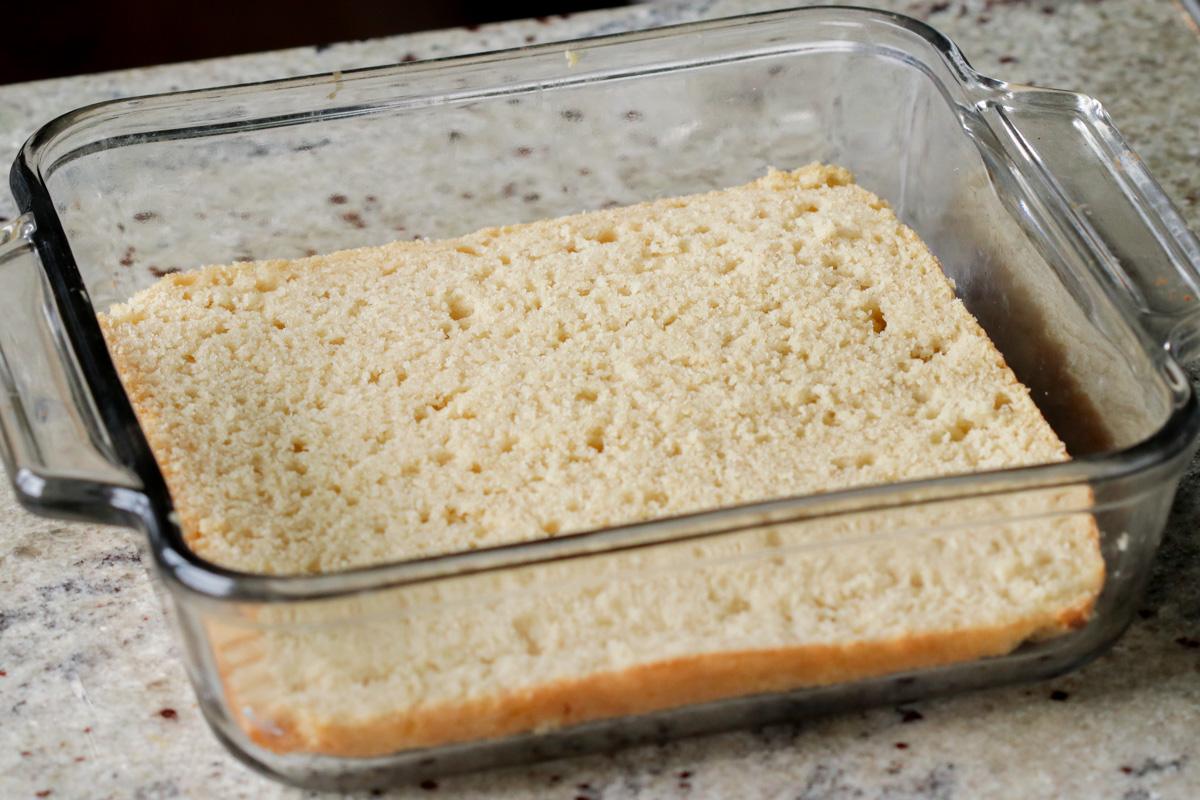 tiramisu cake layer after slicing in half and poking holes, placed into the baking pan