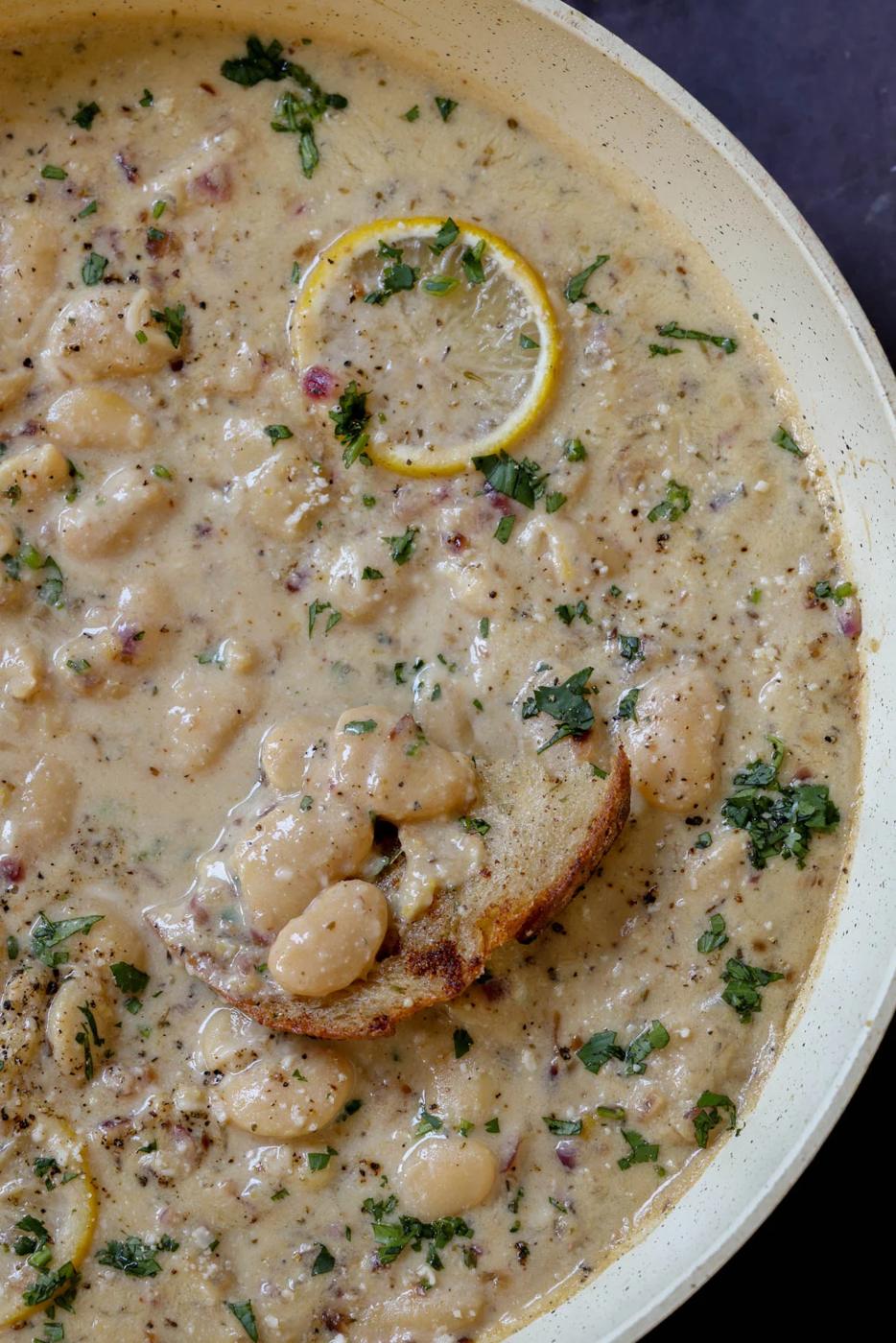 close-up of dipping bread into lemon garlic butter beans in a pan