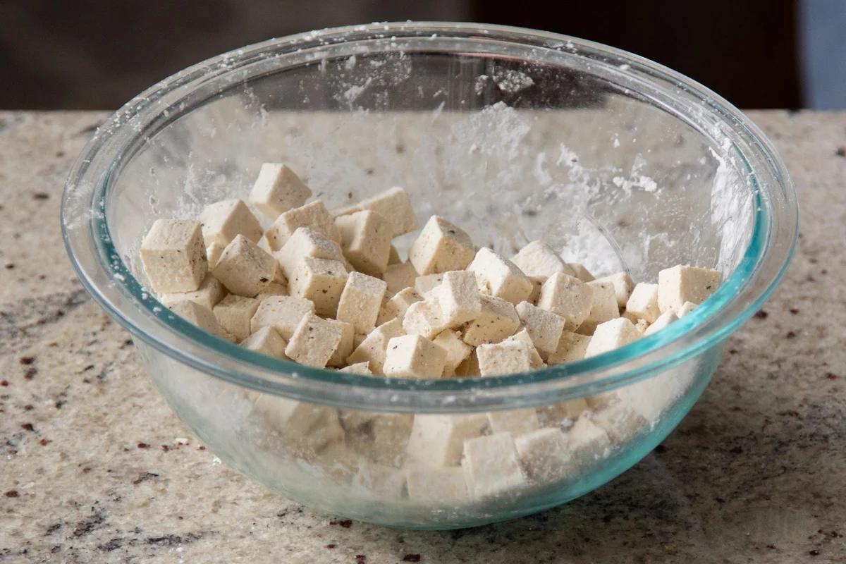 cubed tofu coated in cornstarch in a glass bowl