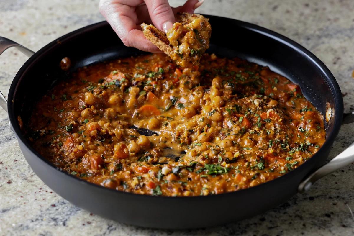 dipping a piece of toast into lentil chickpea stew