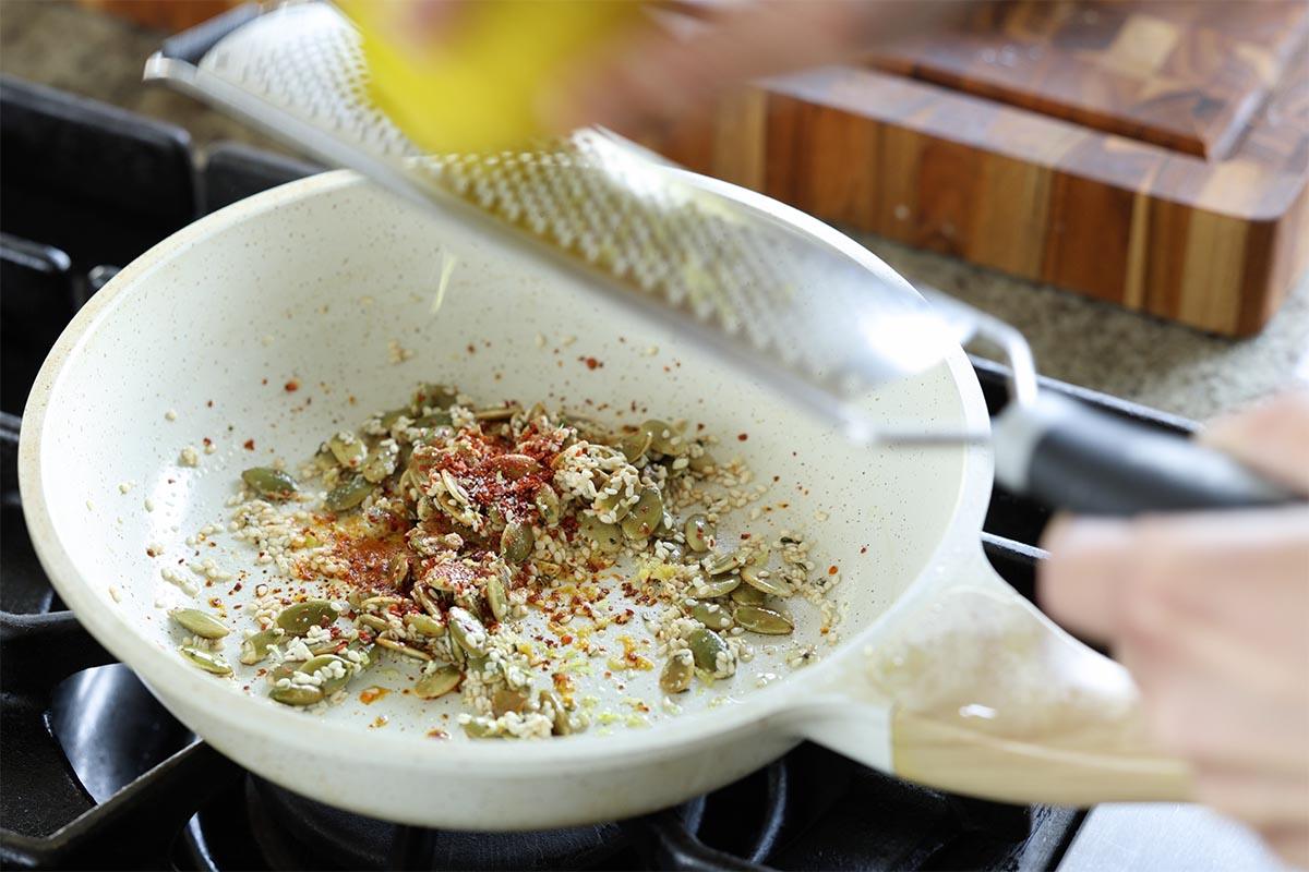 adding pepper flakes and lemon zest to the seeds in the pan