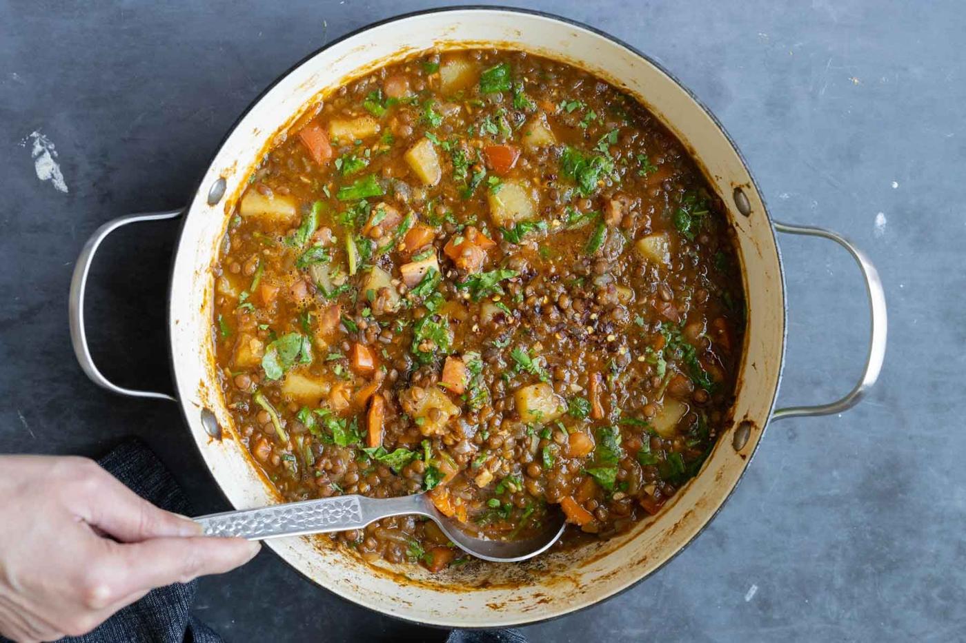 spoon serving some lentil potato soup from the pot