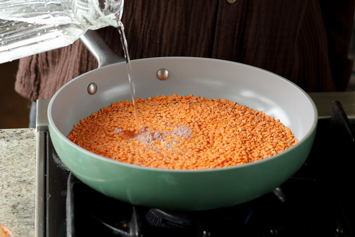 adding red lentils and water to the pan