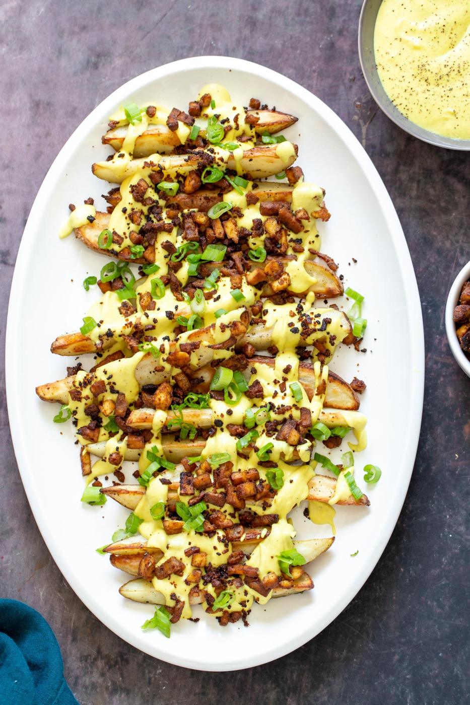 loaded baked potato wedges on a a platter topped with vegan cheese sauce and tofu bacon