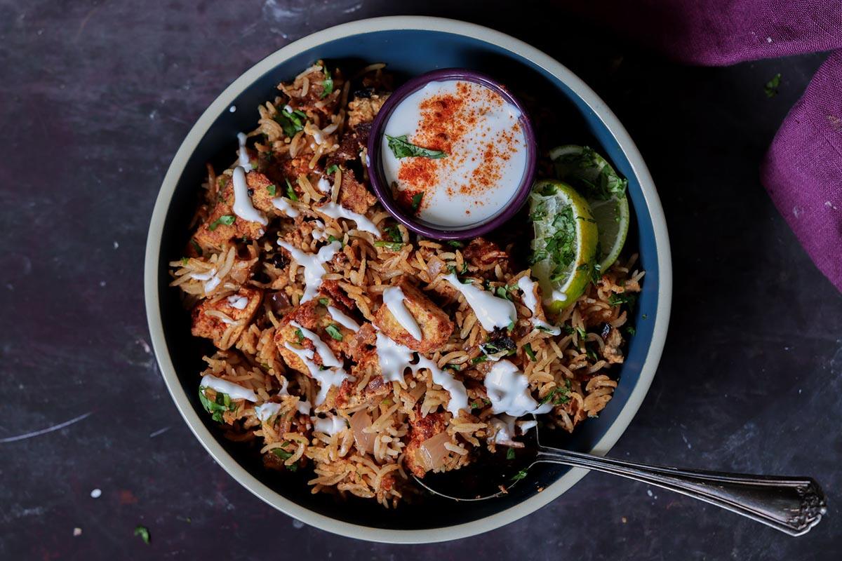 Lucknowi biryani in a bowl topped with raita and a ramekin of raita on the side